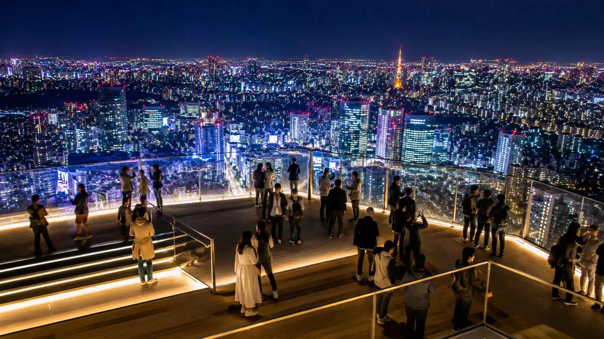 Guide pointing out the illuminated Tokyo skyline from Shibuya Sky's observation deck at night, Shibuya Sky night tour